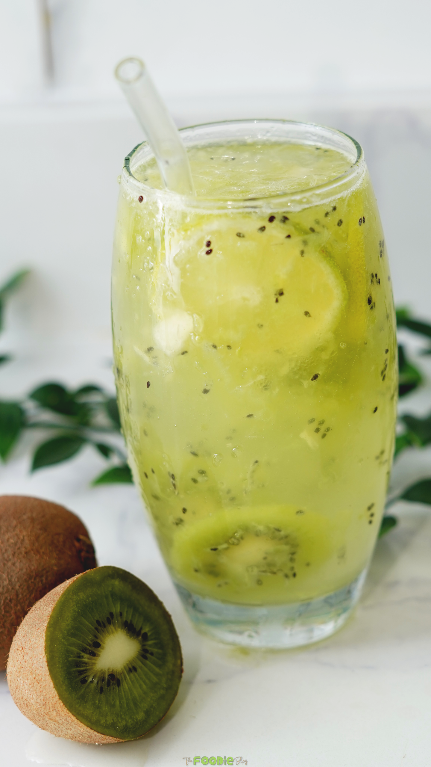 Tall glass of green kiwi drink with fresh kiwi pieces, lime, and soda bubbles.