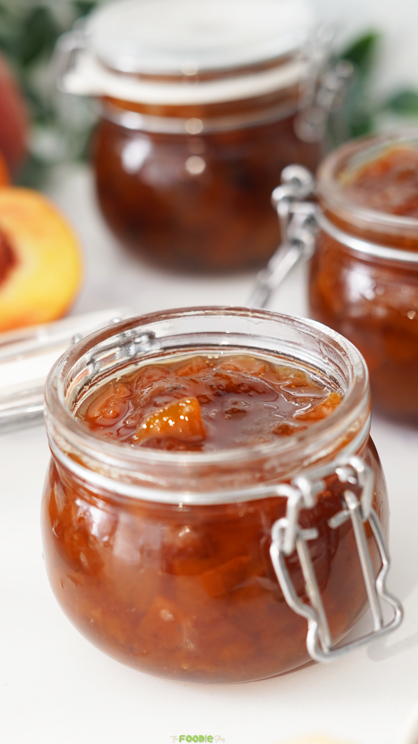 Homemade peach preserves in glass jars with fresh peaches in the background.