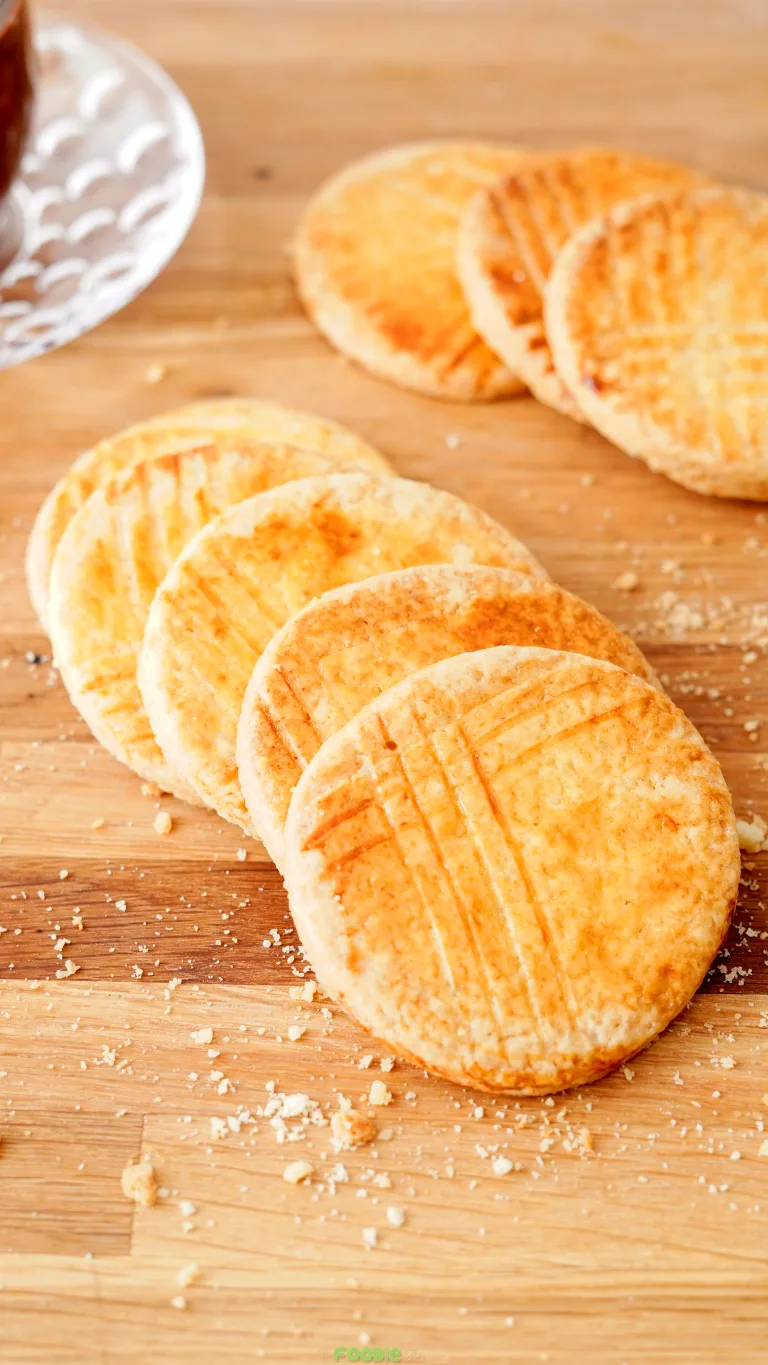 Round Galettes Bretonnes arranged on a wooden board with golden tops and fork marks.