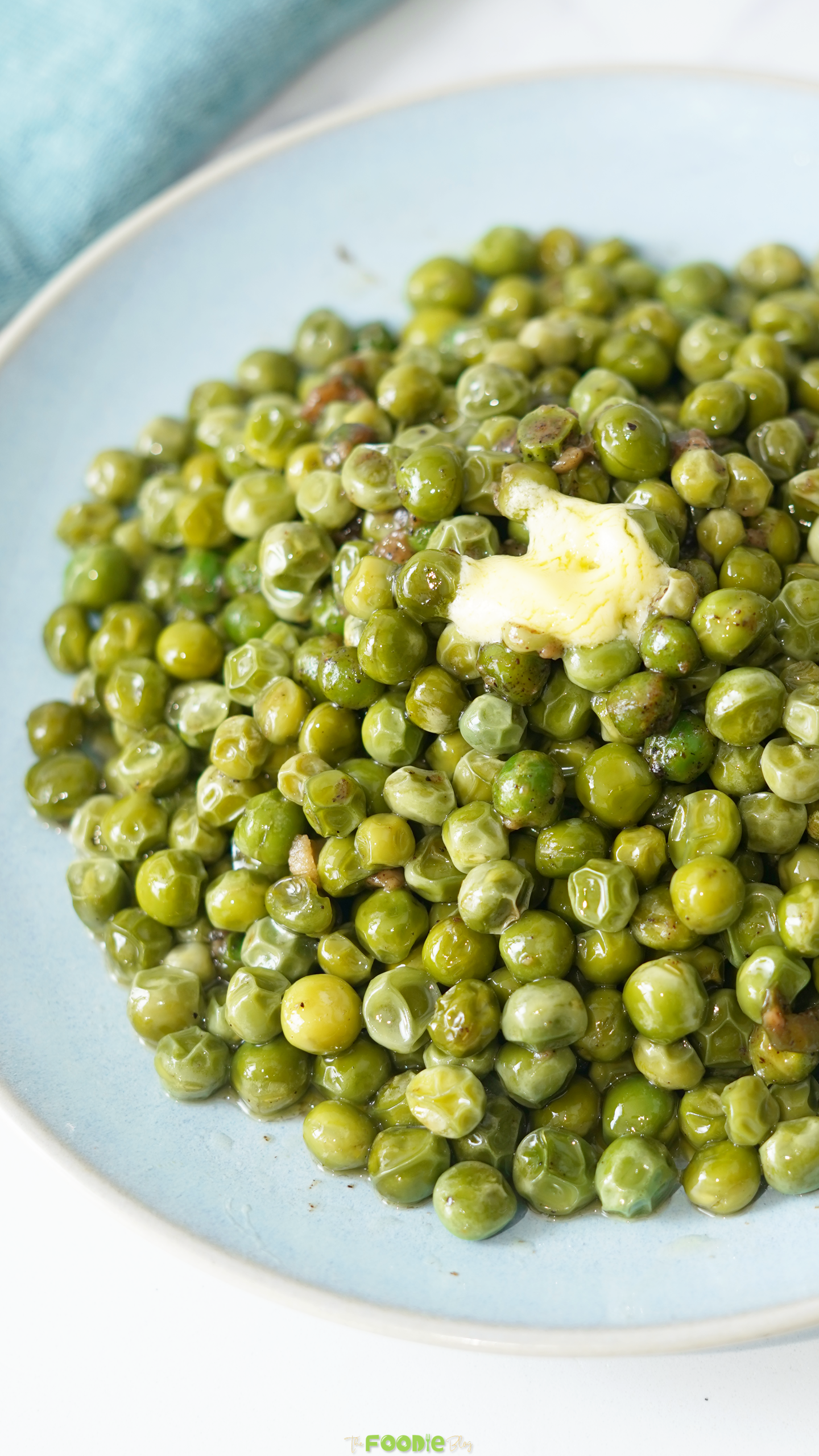 Close-up of tender green peas coated in garlic butter with a small pat of butter on top.