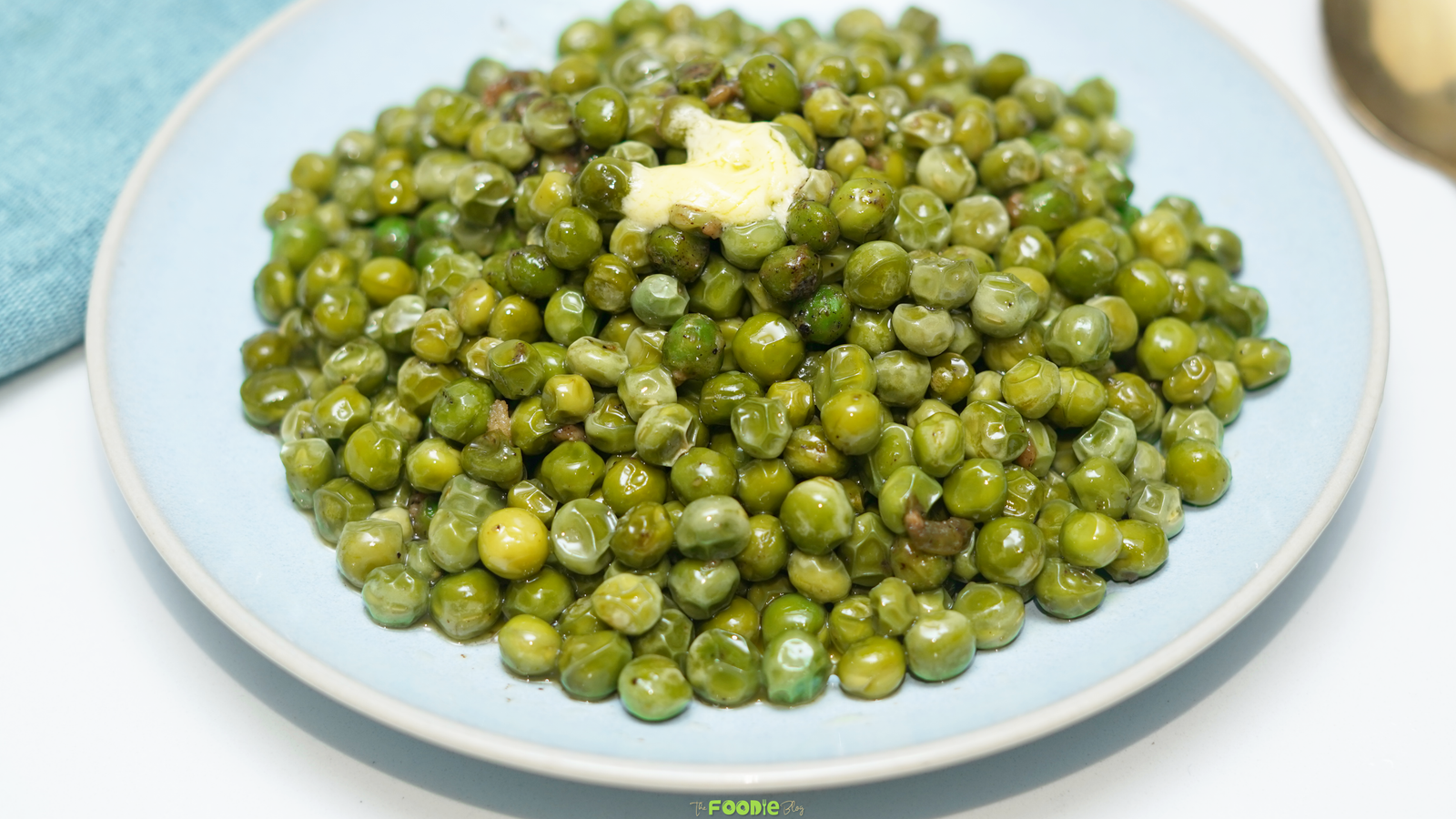 Garlic buttered peas piled on a light blue plate with a pat of butter and minced garlic.