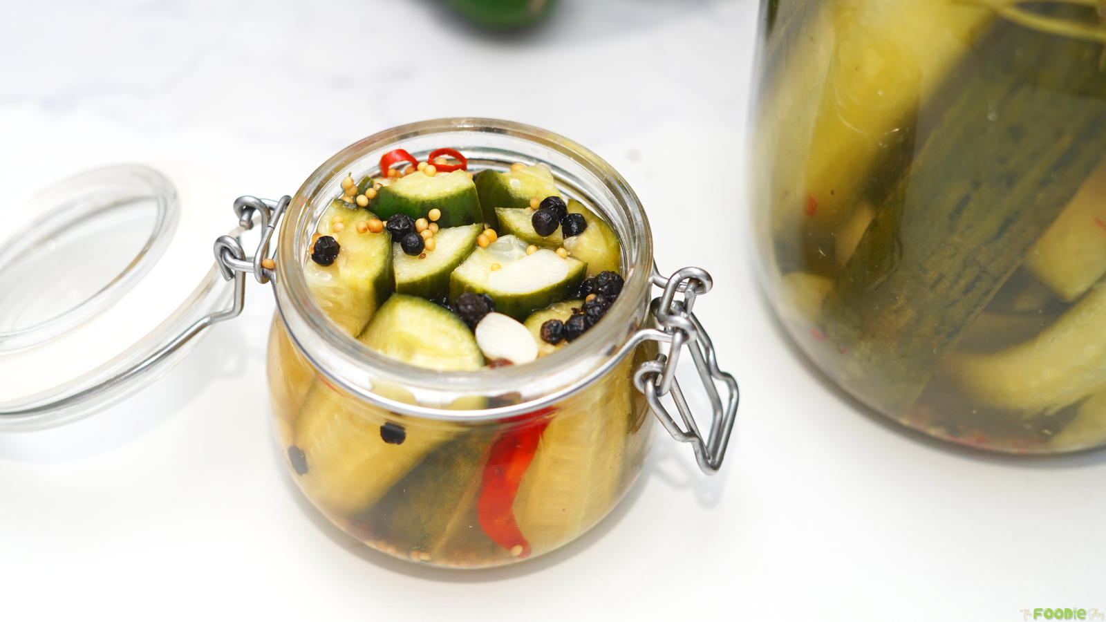 Small glass jar of garlic dill refrigerator pickles with mustard seeds, peppercorns, and sliced red chili.