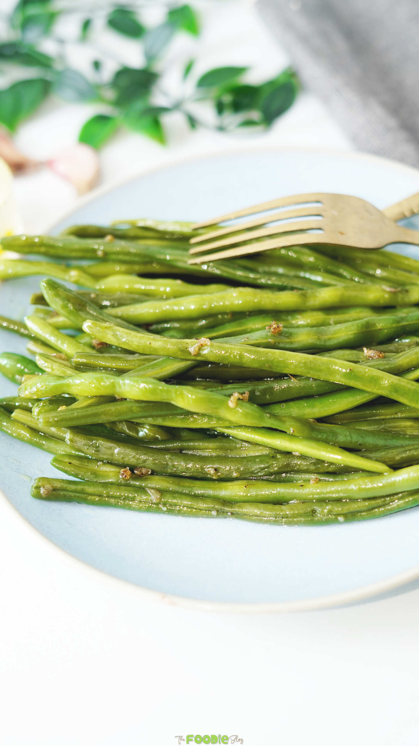 Close-up of sautéed green beans with golden garlic pieces and a fork.