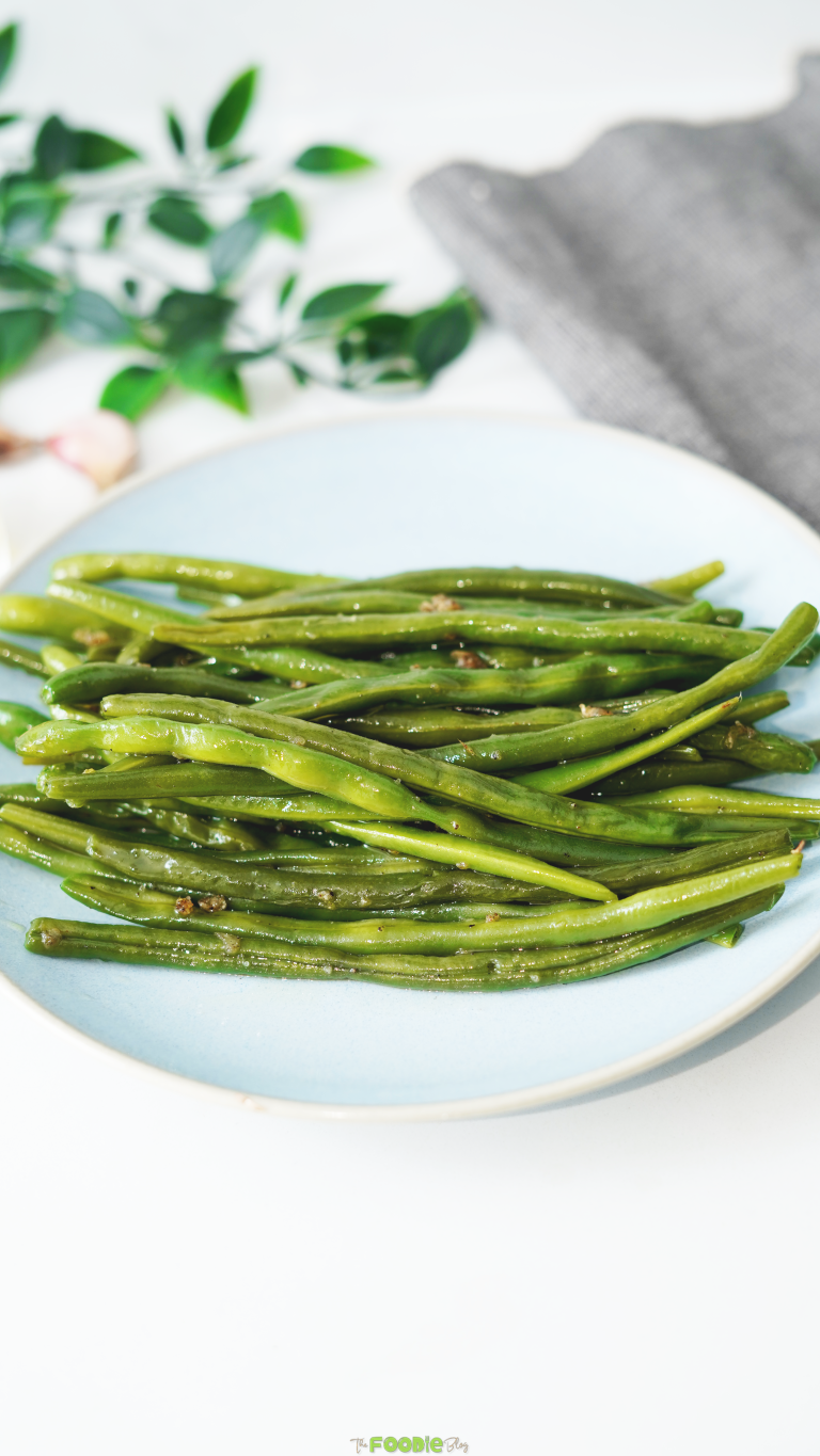 Glossy sautéed green beans with garlic served on a light blue plate.