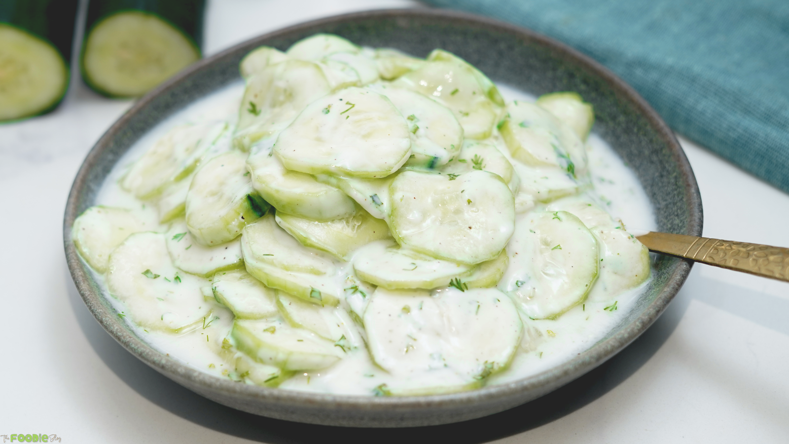 Creamy German cucumber salad with thin cucumber slices, sour cream dressing, and fresh dill in a gray bowl.