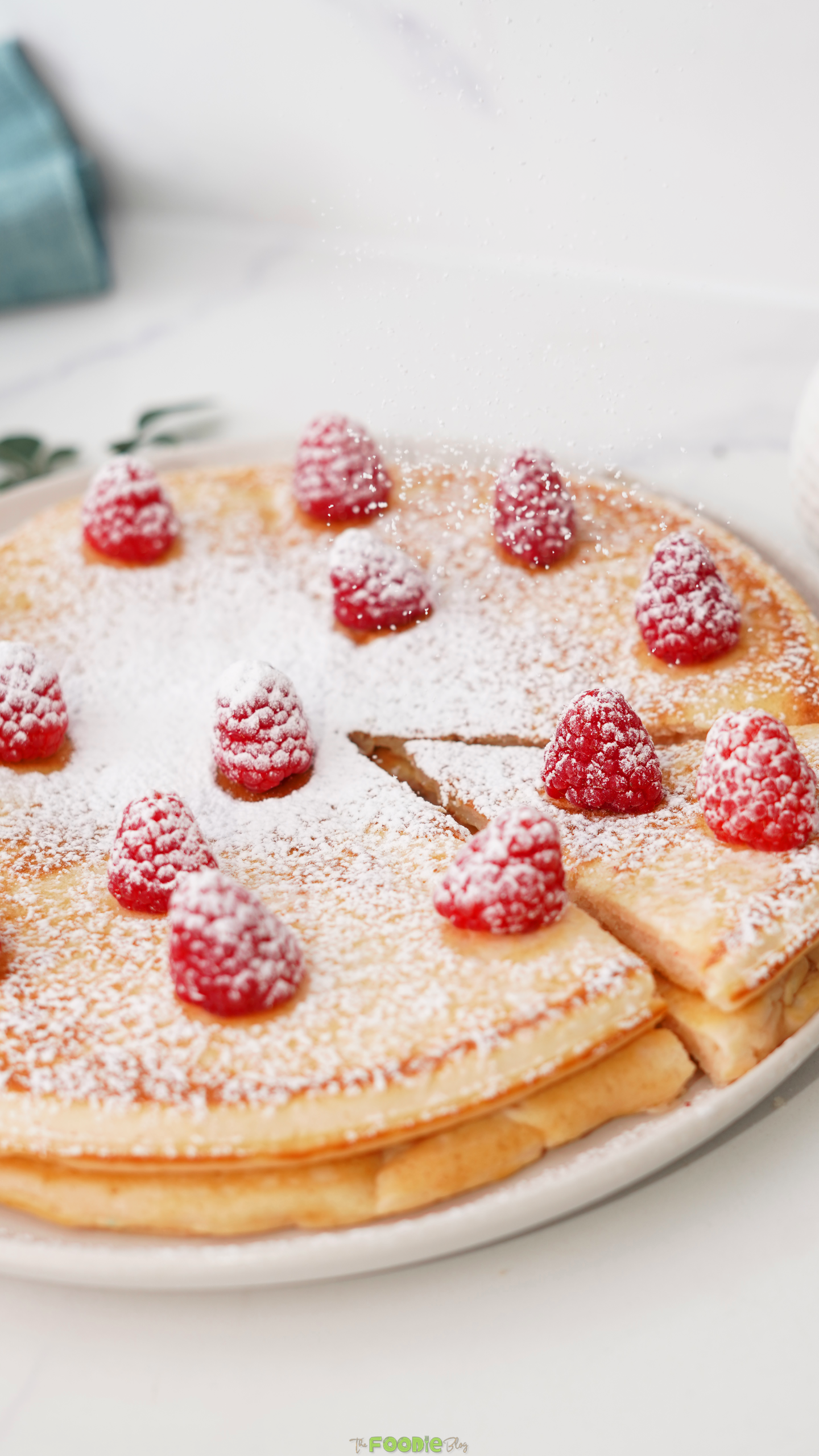 Stack of Giant Pancakes topped with fresh raspberries and powdered sugar.