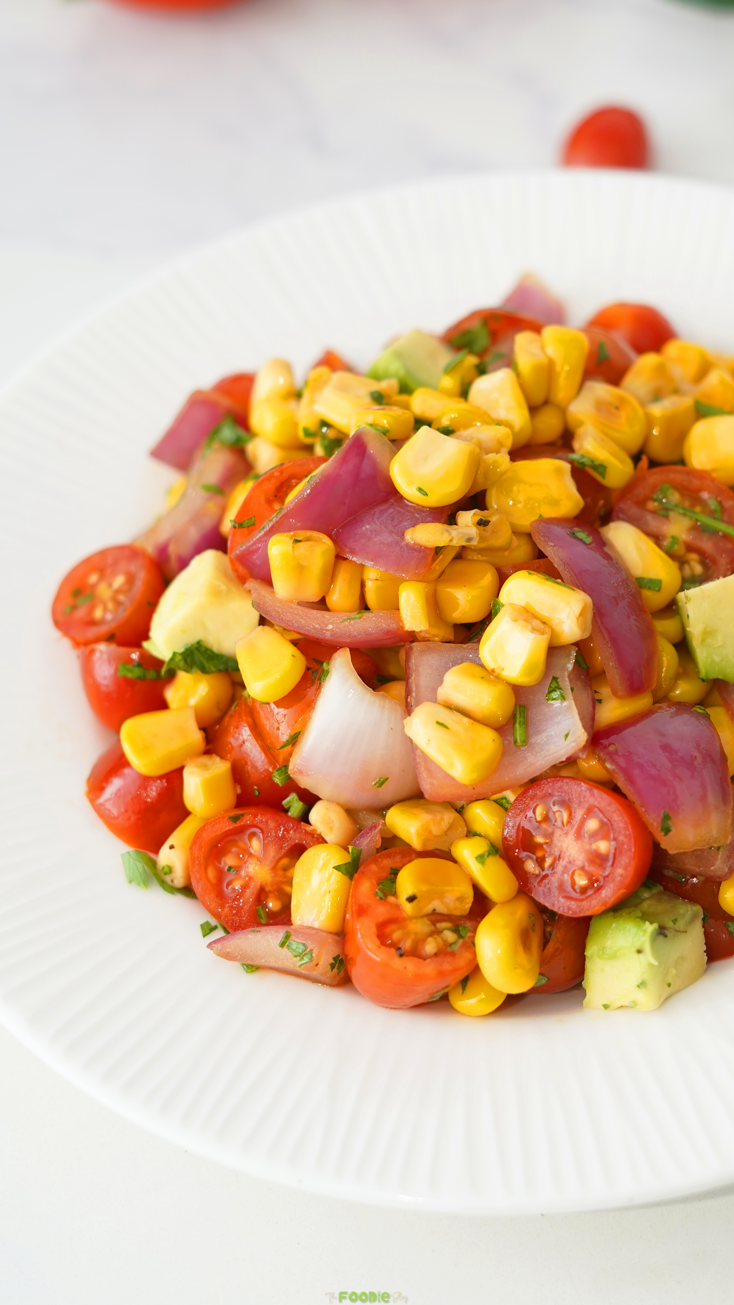 Close-up of grilled corn avocado salad with cherry tomatoes, red onion, parsley, and lime dressing.