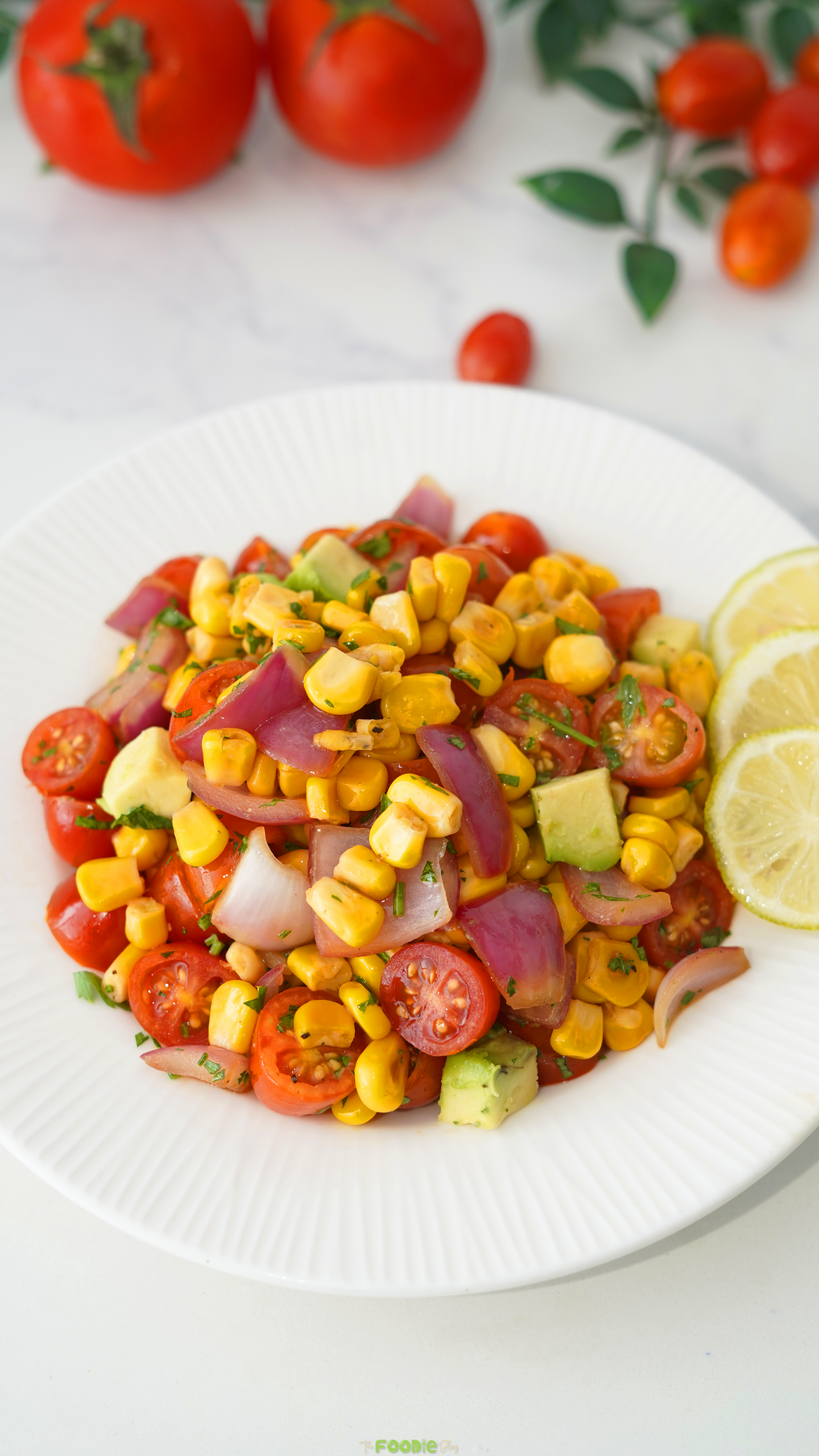 Grilled corn salad with avocado, cherry tomatoes, red onion, parsley, and fresh lime on a white plate.