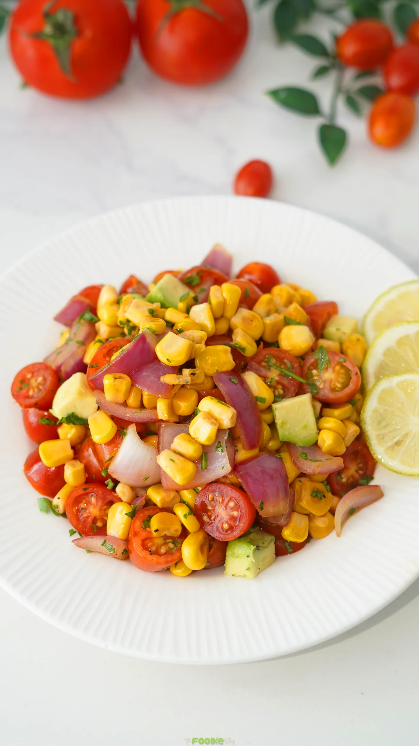 Grilled corn salad with avocado, cherry tomatoes, red onion, parsley, and fresh lime on a white plate.