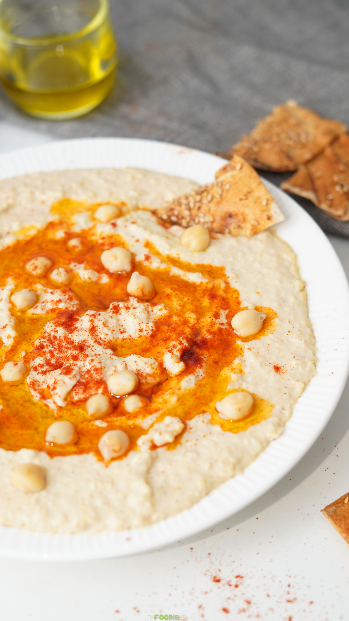 Smooth hummus dip with paprika, olive oil, chickpeas, and crunchy pita chips on the side.