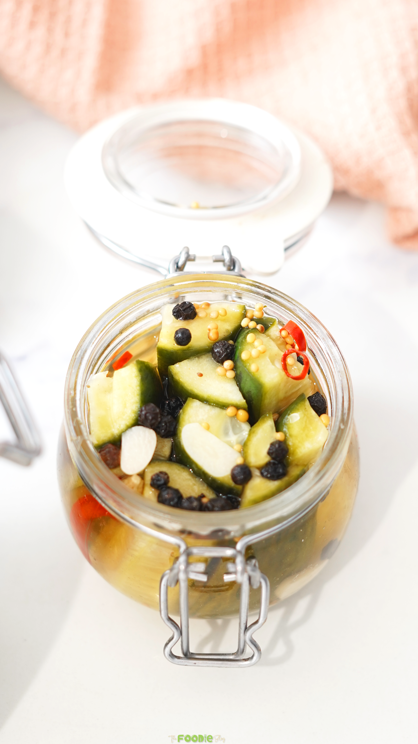 Chopped refrigerator dill pickles in a glass jar with garlic, mustard seeds, peppercorns, and red chili.