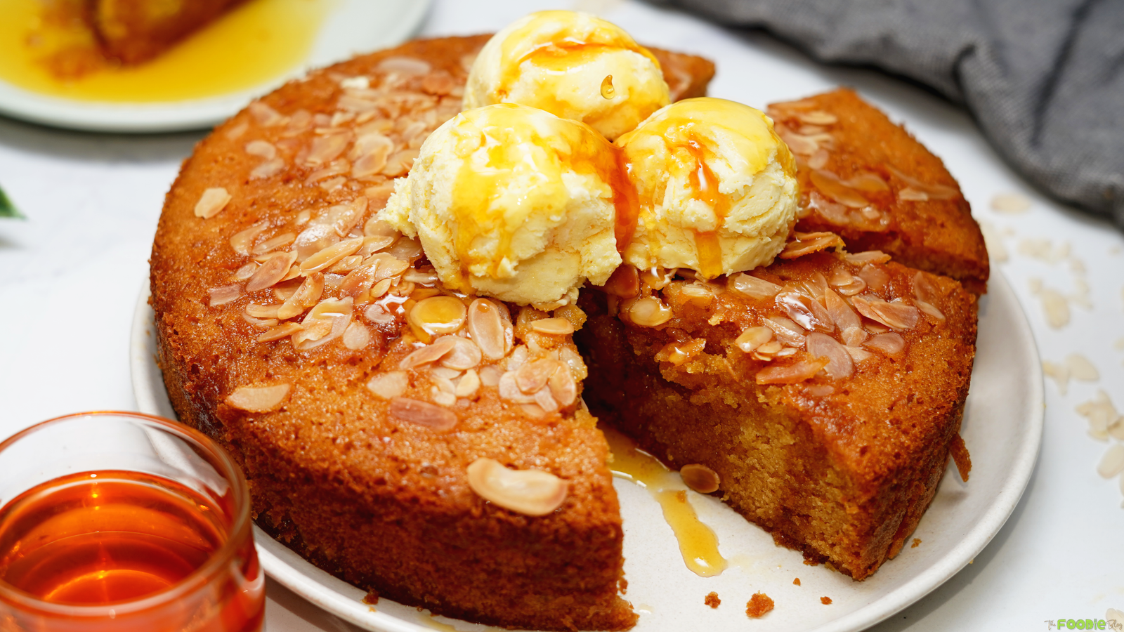 Warm honey cake with sliced almonds, vanilla ice cream, and honey syrup on a white plate.