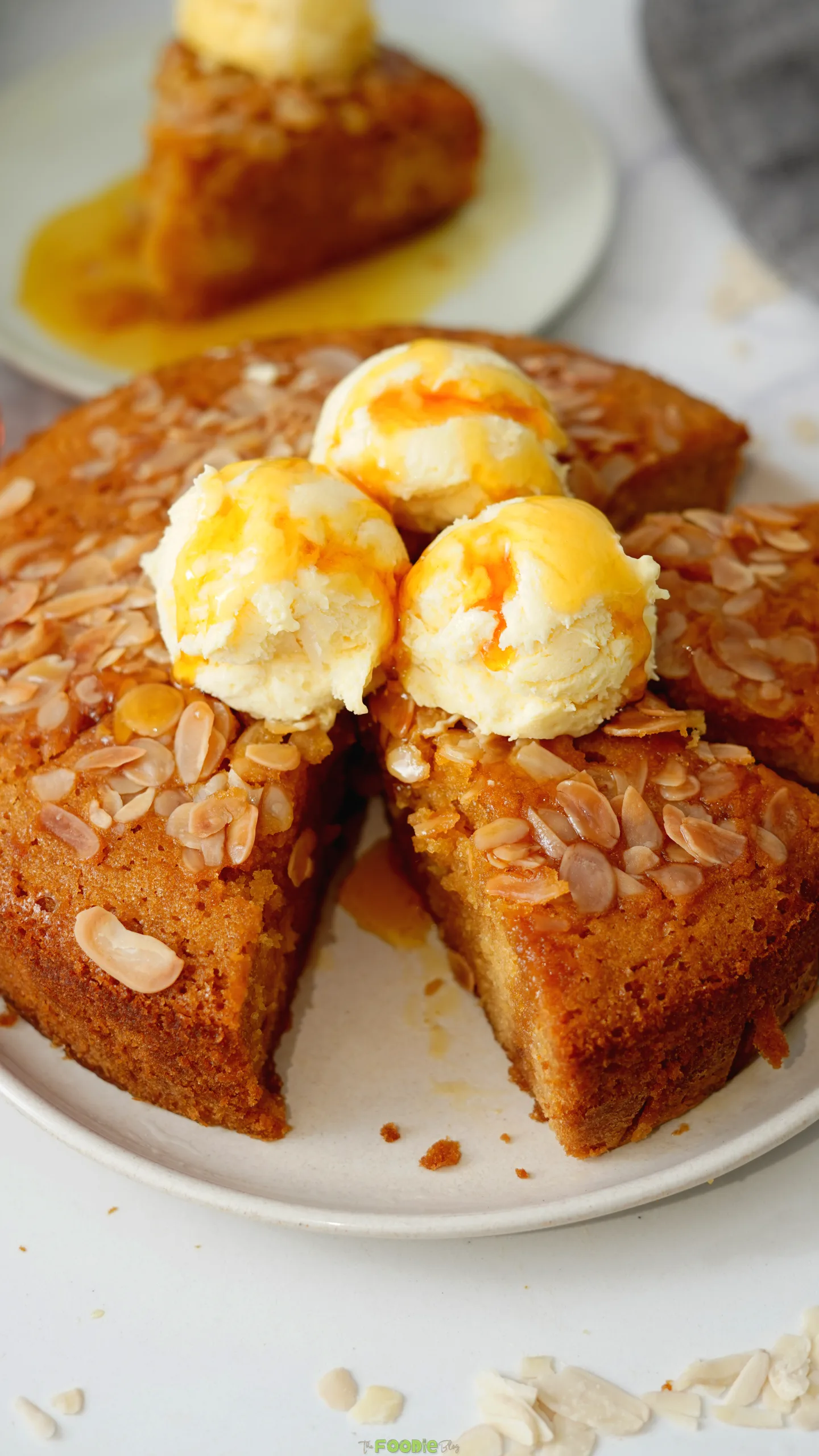 Slice of warm Honey Cake topped with vanilla ice cream, sliced almonds, and honey drizzle.