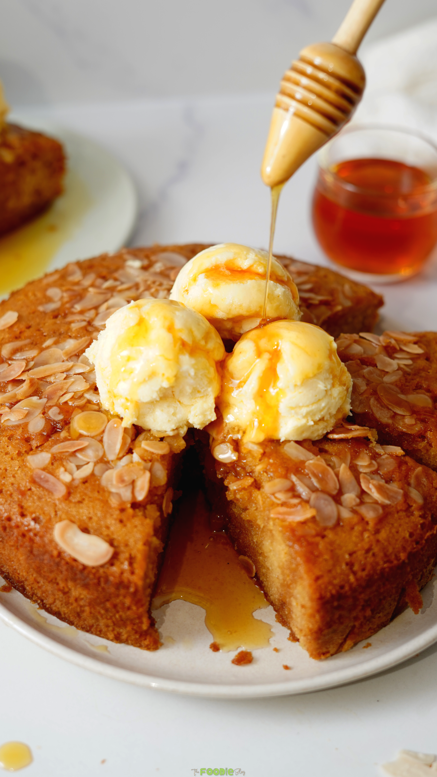 Honey drizzling from a dipper over vanilla ice cream and sliced almond Honey Cake.