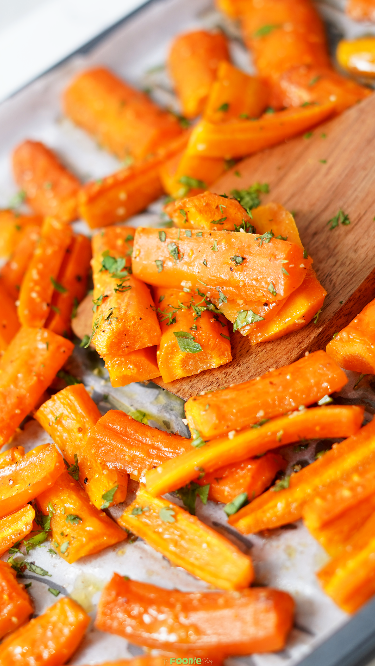 Honey Roasted Carrots on a baking sheet with a wooden spatula and chopped herbs.
