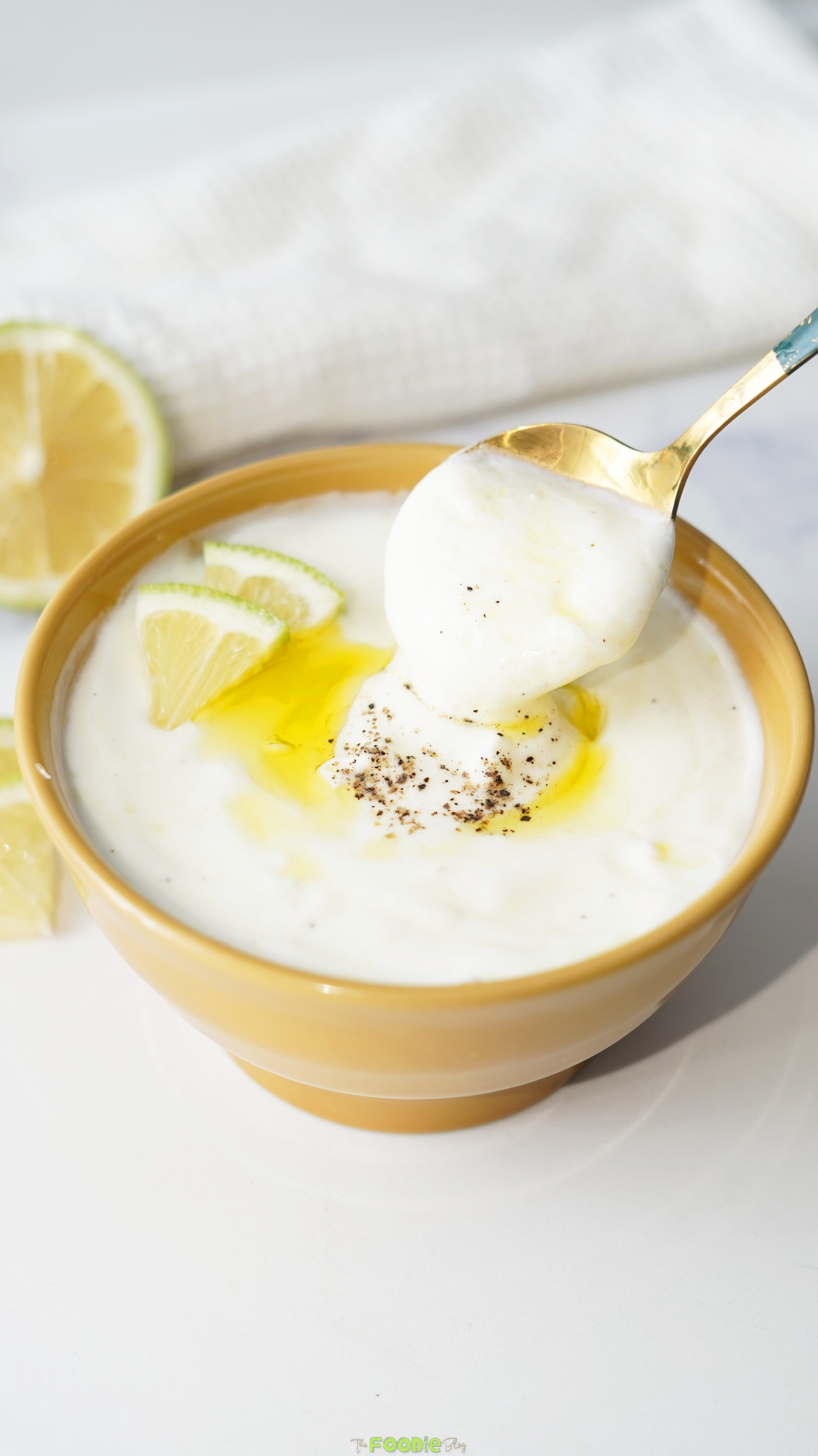 Creamy lemon garlic yogurt sauce in a yellow bowl with a spoon, olive oil, and black pepper.