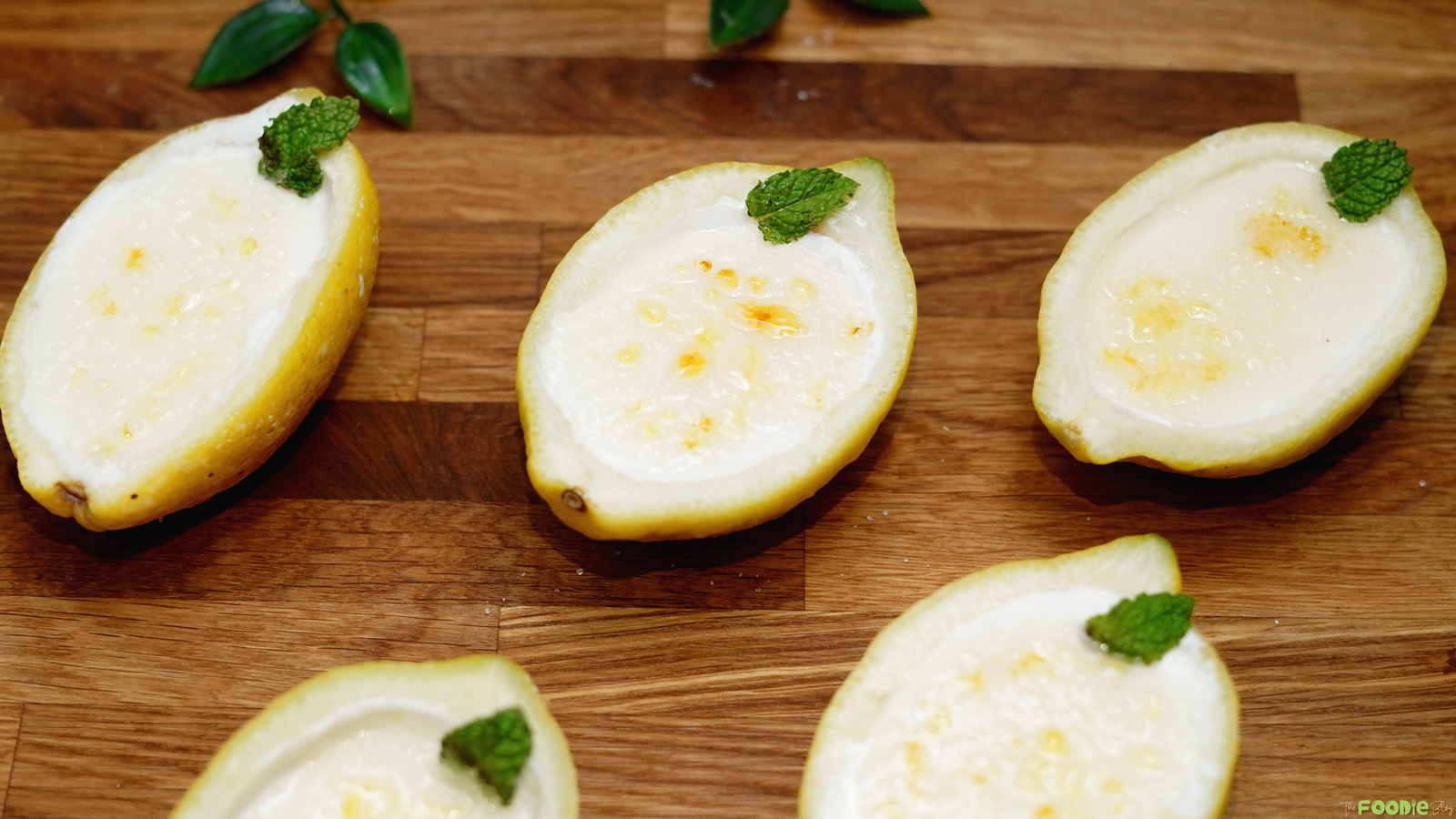 Lemon posset brûlée served in hollow lemon shells with caramelized sugar and fresh mint.