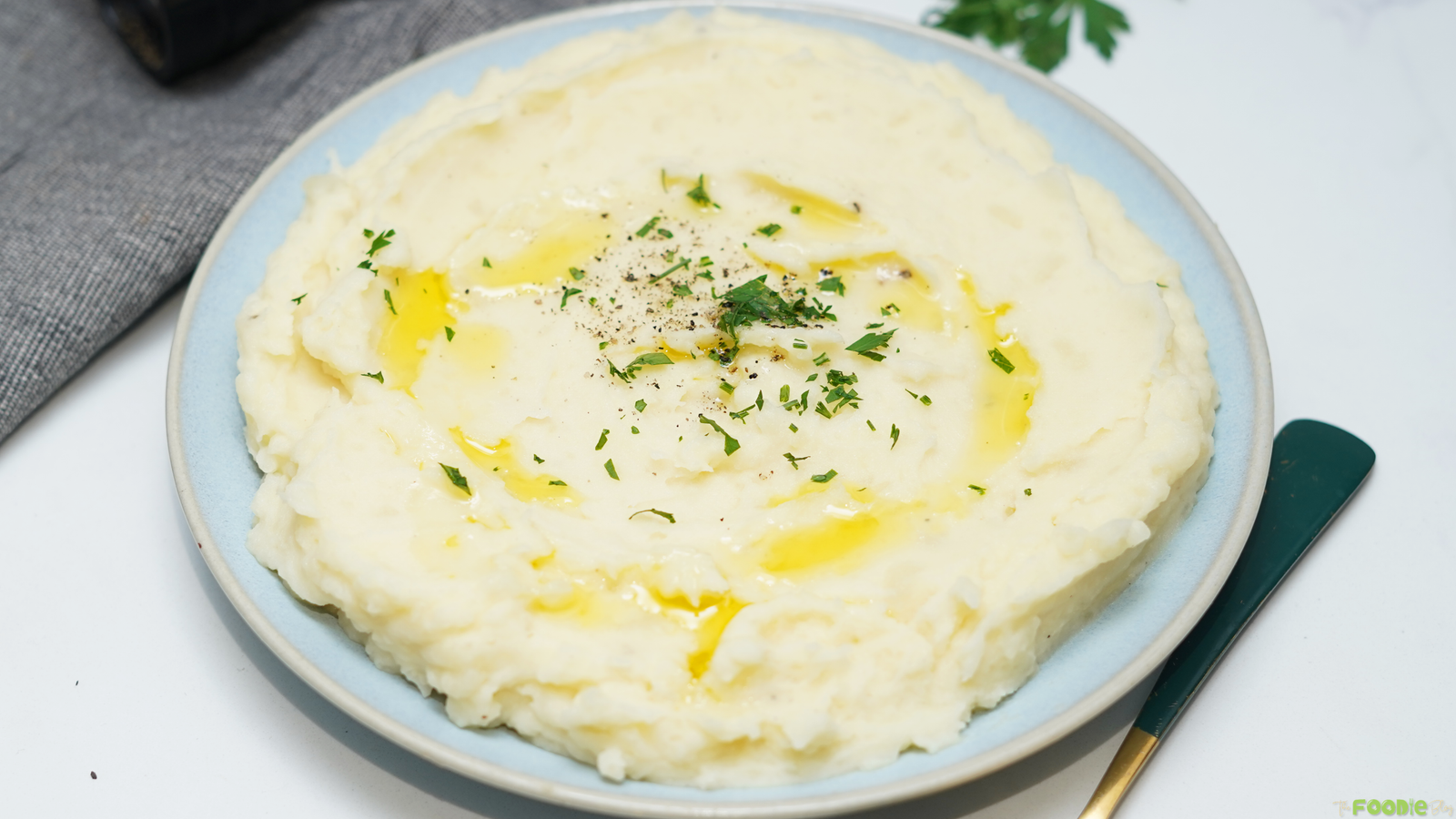Make ahead mashed potatoes served in a shallow bowl with butter, herbs, and black pepper.