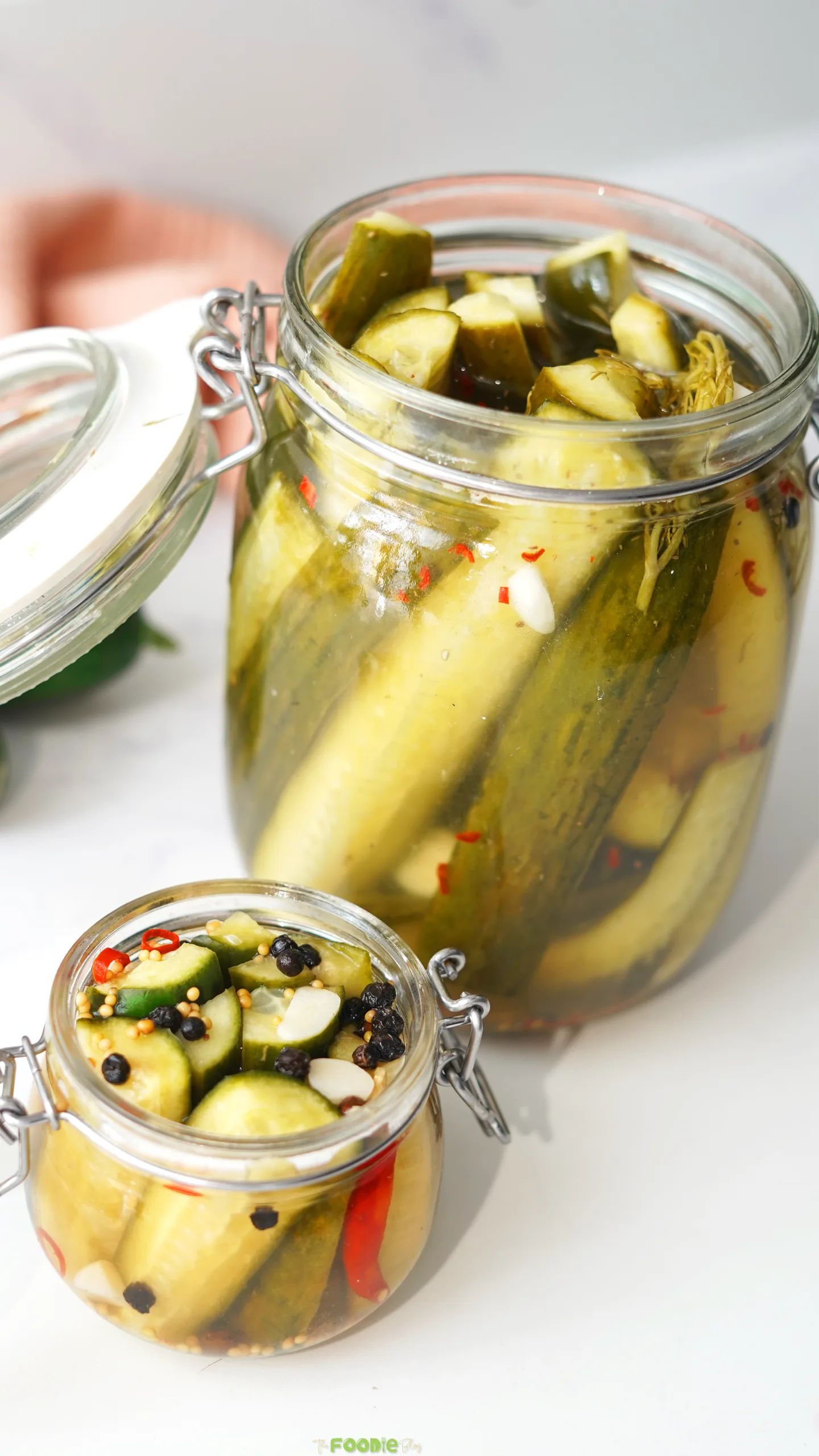 Two glass jars filled with crisp refrigerator dill pickles, fresh dill, garlic, pickling spices, and red chili.