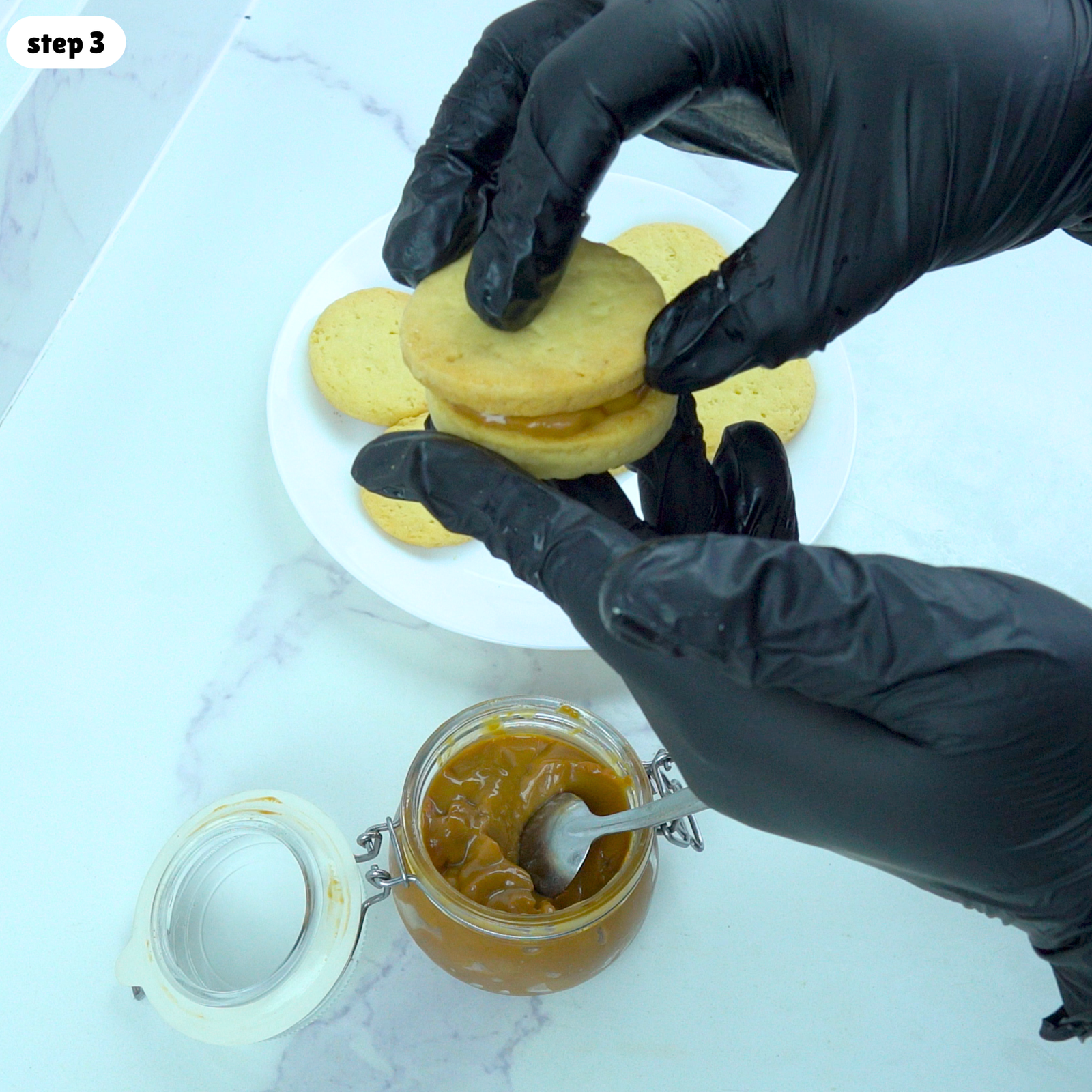 Hands filling shortbread cookies with dulce de leche to make sandwich cookies.