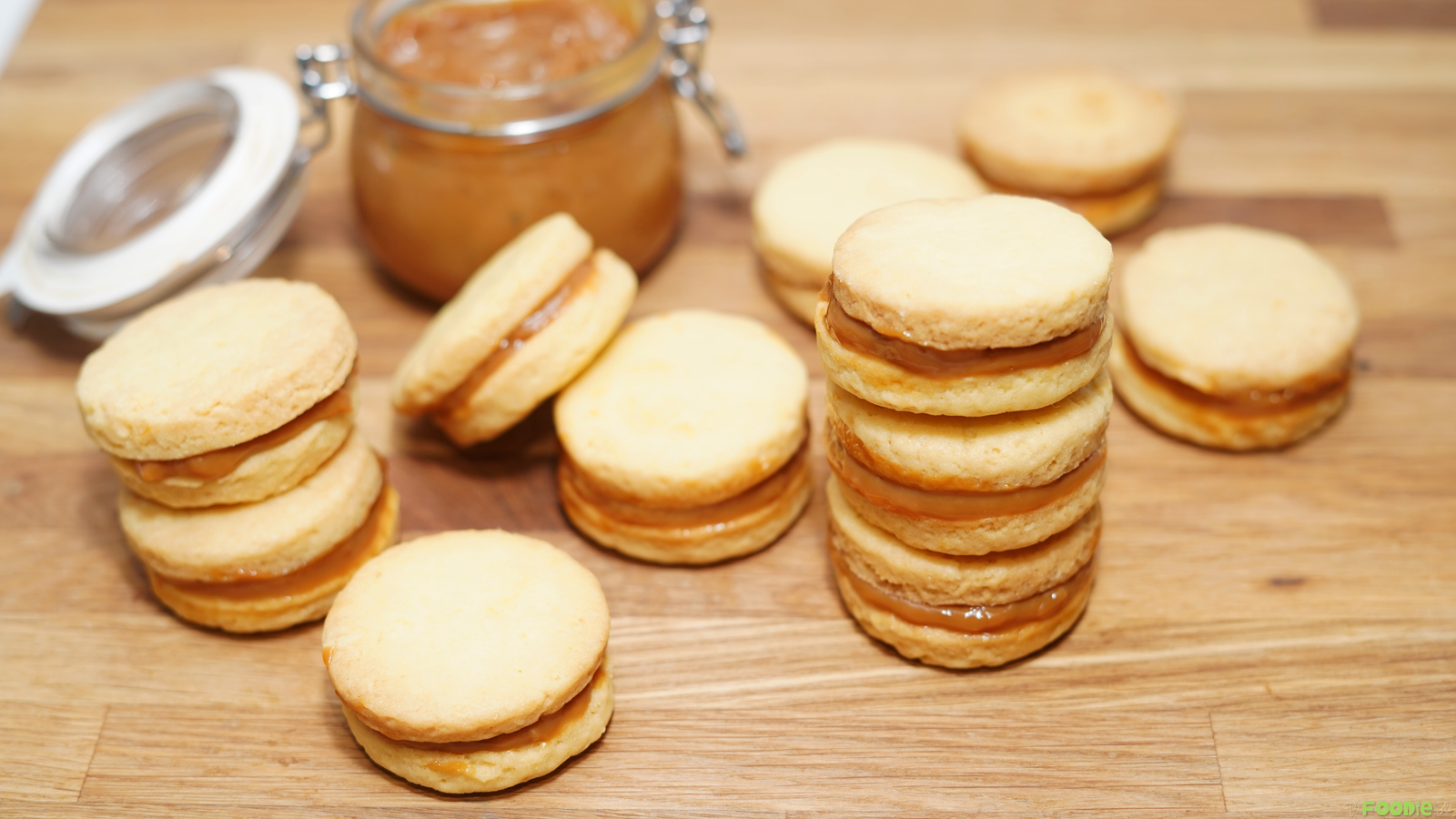 Shortbread cookie sandwiches filled with dulce de leche on a wooden board.