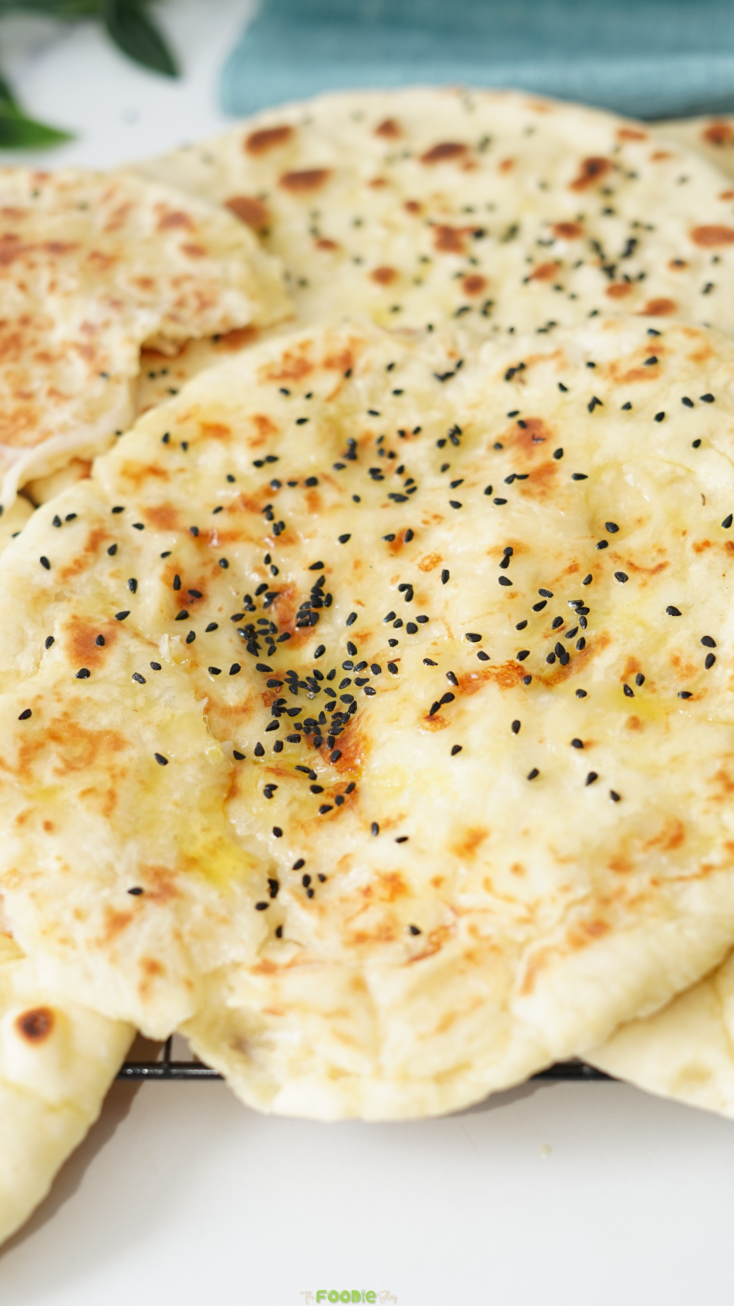 Close-up of soft cheese naan brushed with melted butter and sprinkled with black sesame seeds.