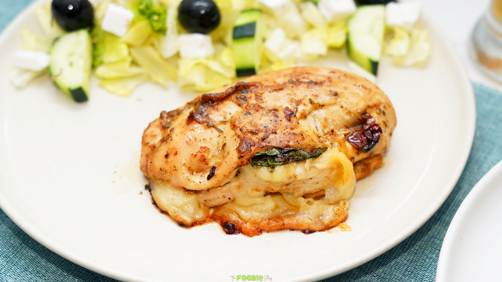 Golden baked chicken breast stuffed with melted mozzarella, spinach, and sun-dried tomatoes served on a white plate.