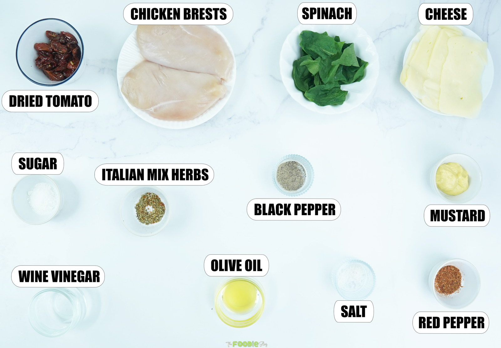Ingredients for sun-dried tomato spinach and cheese stuffed chicken breast arranged on a white marble surface.