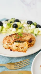 Vertical image of baked chicken breast stuffed with spinach, mozzarella cheese, and sun-dried tomatoes.