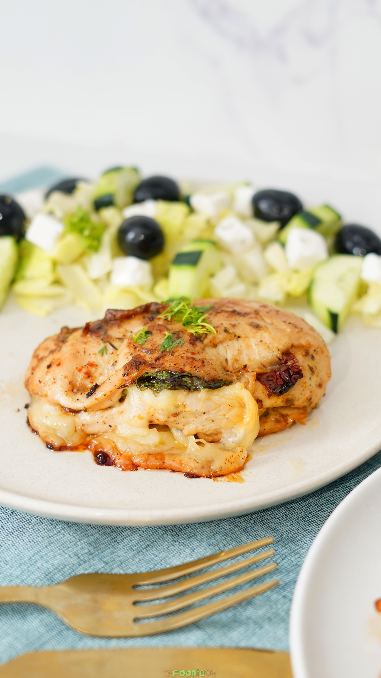 Vertical image of baked chicken breast stuffed with spinach, mozzarella cheese, and sun-dried tomatoes.