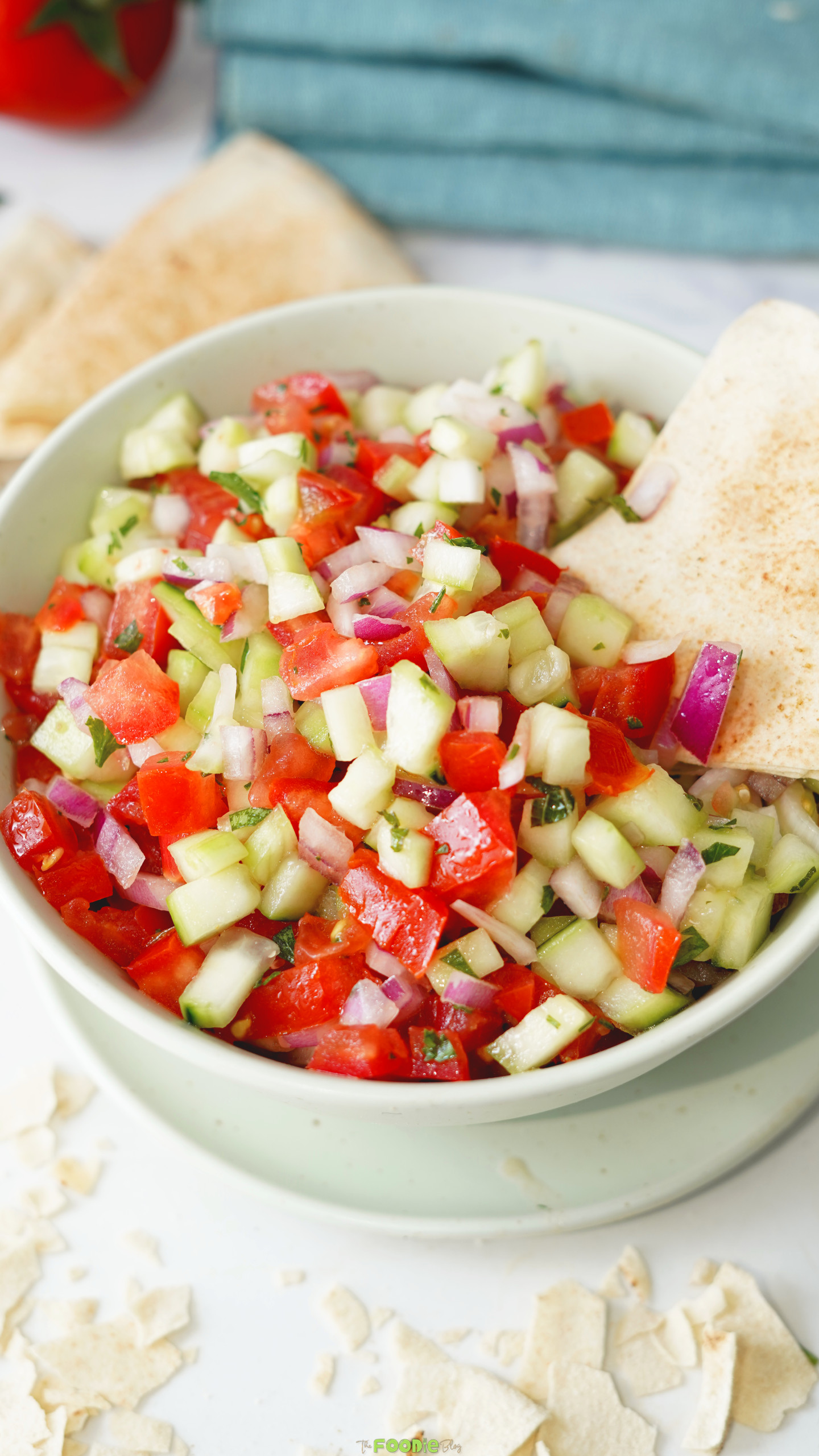 Fresh tomato cucumber salad with red onion, mint, parsley, and pita chips in a bowl.