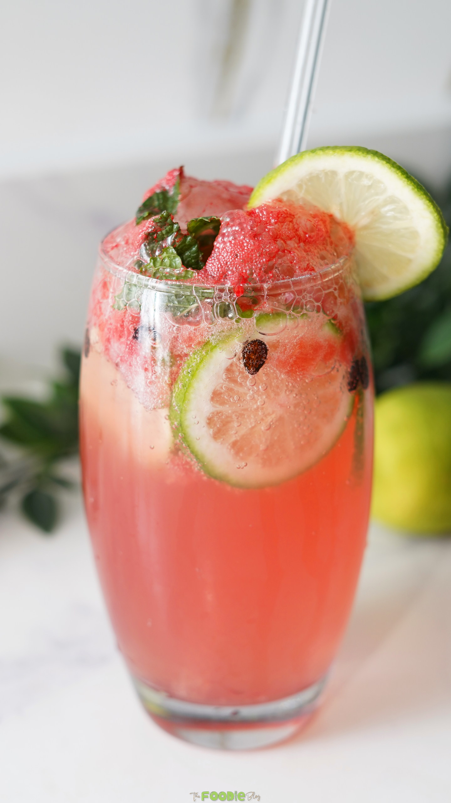 Pink watermelon mojito mocktail in a tall glass with lime slices, fresh mint, watermelon, and bubbles.