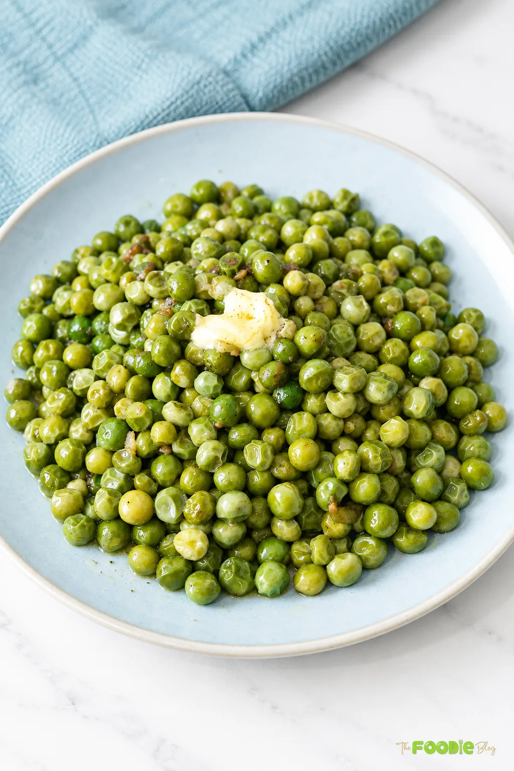 Garlic butter peas served on a light blue plate with melted butter on top