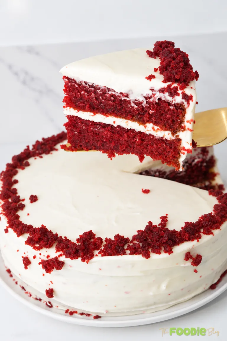 Slice of red velvet cake with cream cheese frosting lifted above the whole cake