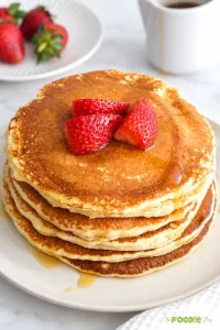 Stack of protein pancakes topped with strawberries and maple syrup