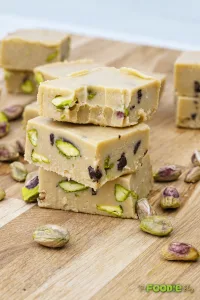 Creamy tahini fudge squares with pistachios and chocolate chips stacked on a wooden board