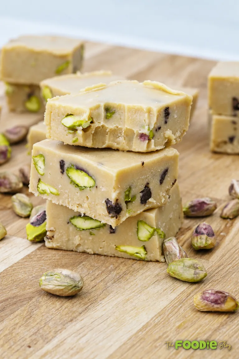 Creamy tahini fudge squares with pistachios and chocolate chips stacked on a wooden board