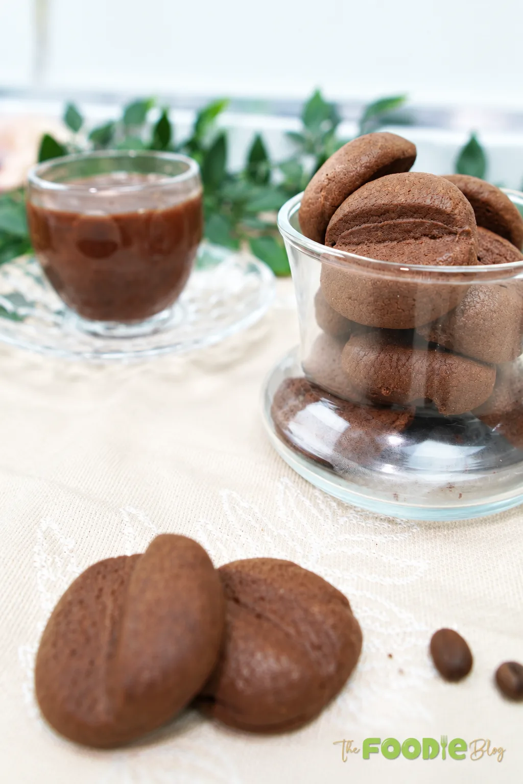 Coffee bean shaped cookies arranged in a glass jar beside a cup of coffee