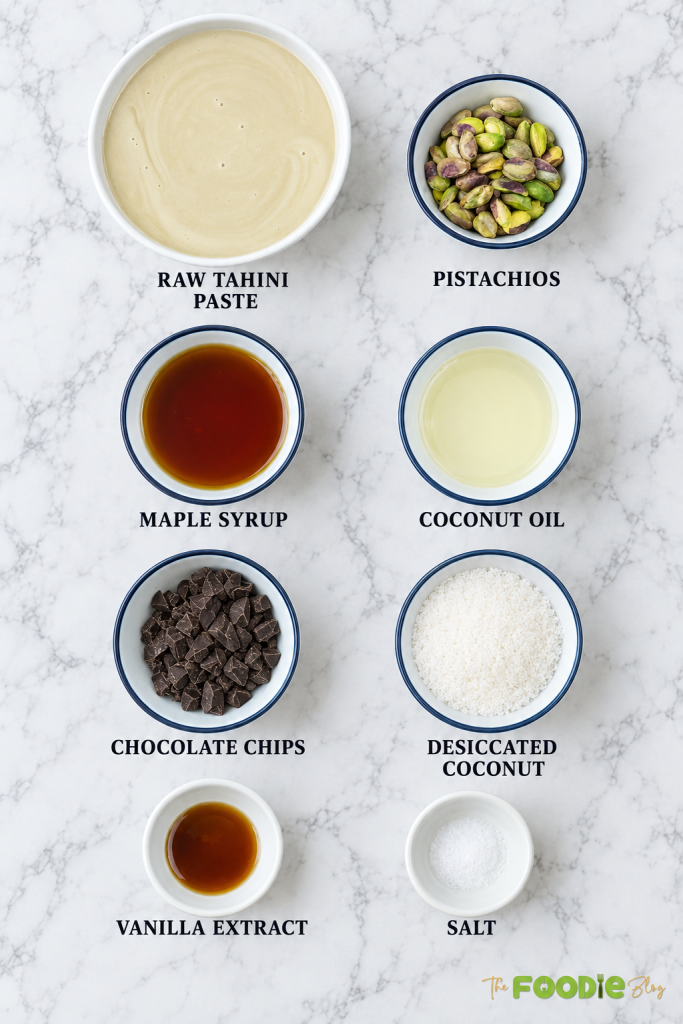 Tahini fudge ingredients including tahini paste, pistachios, maple syrup, coconut oil, chocolate chips, coconut, vanilla, and salt