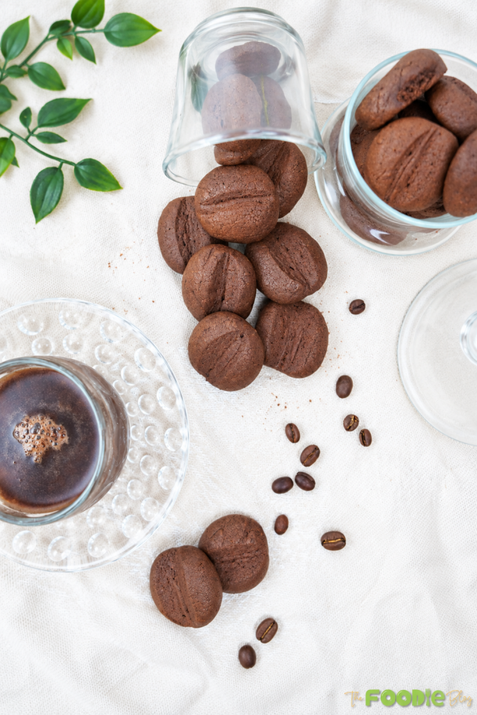 Coffee bean cookies served beside a cup of coffee with scattered coffee beans