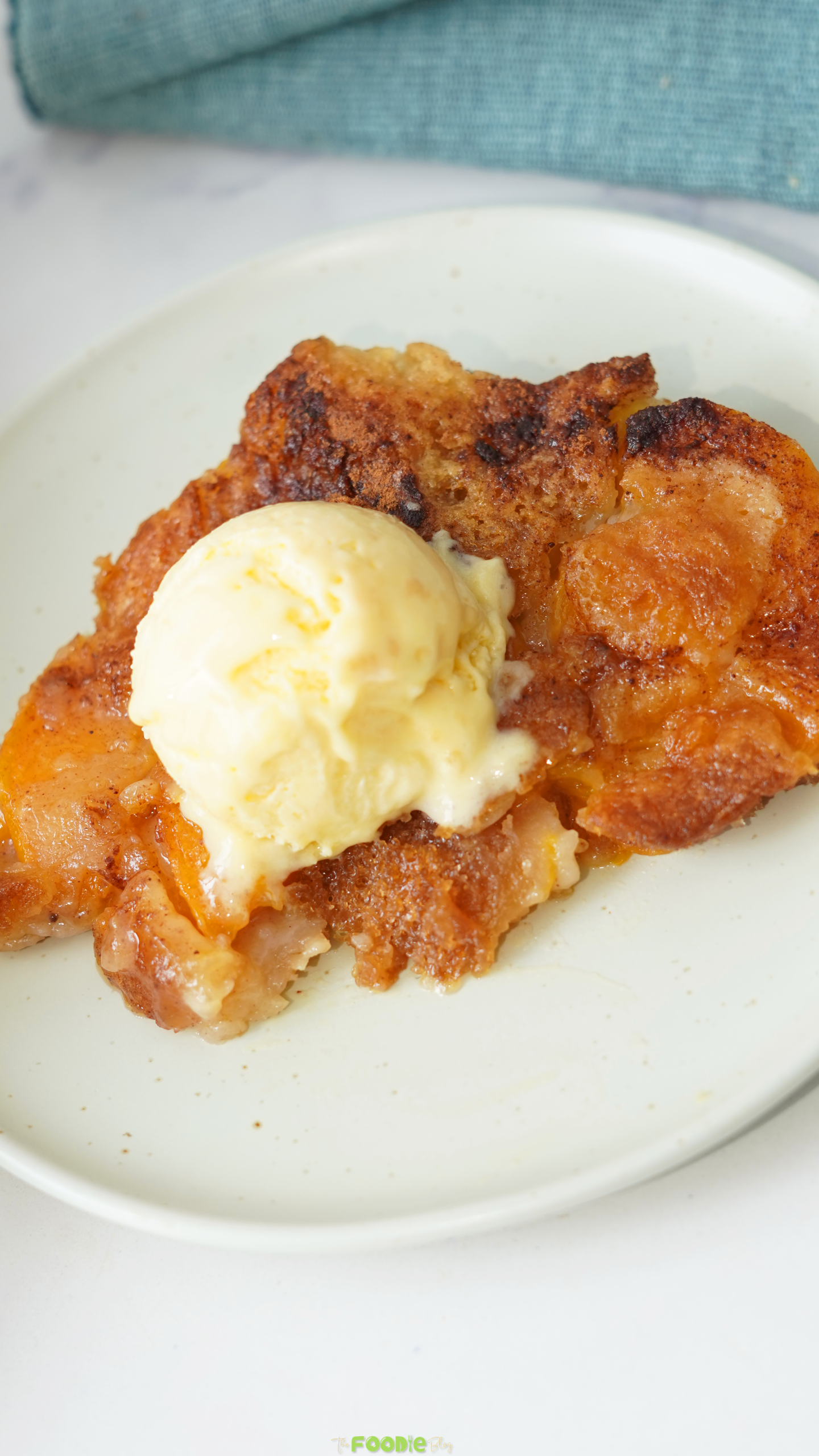 Warm canned peach cobbler served on a plate with a scoop of melting vanilla ice cream.