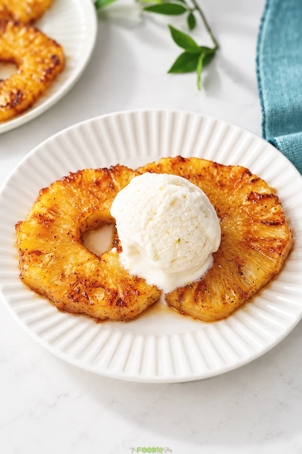 Brown sugar cinnamon grilled pineapple served with vanilla ice cream on a white plate.