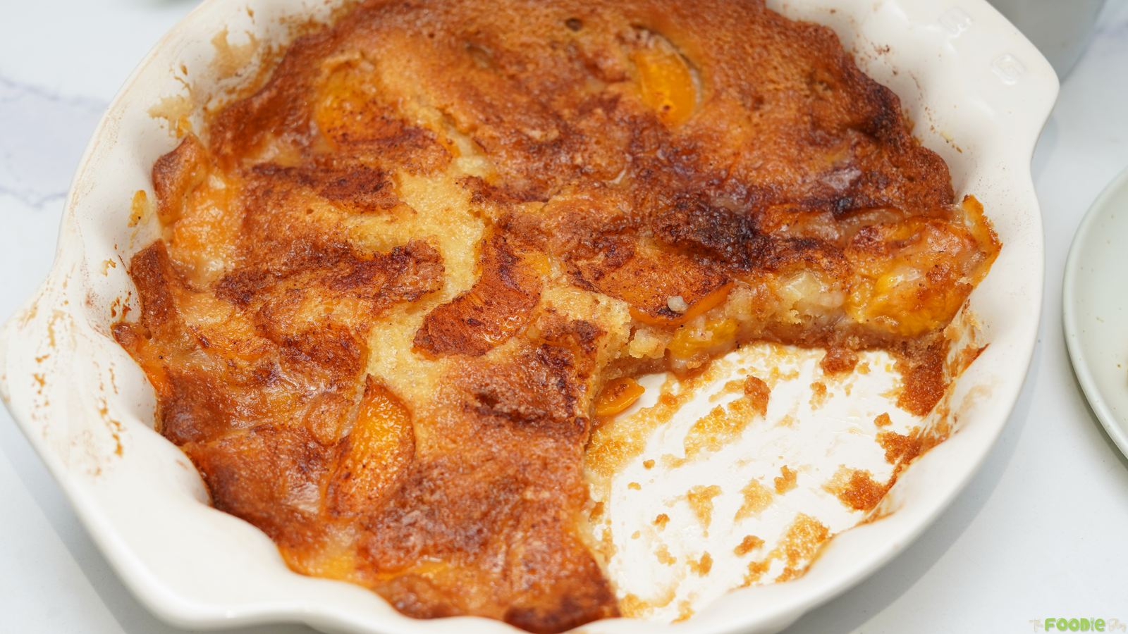 Easy canned peach cobbler baked until golden brown with soft peach slices and a buttery cake-style topping in a white baking dish.
