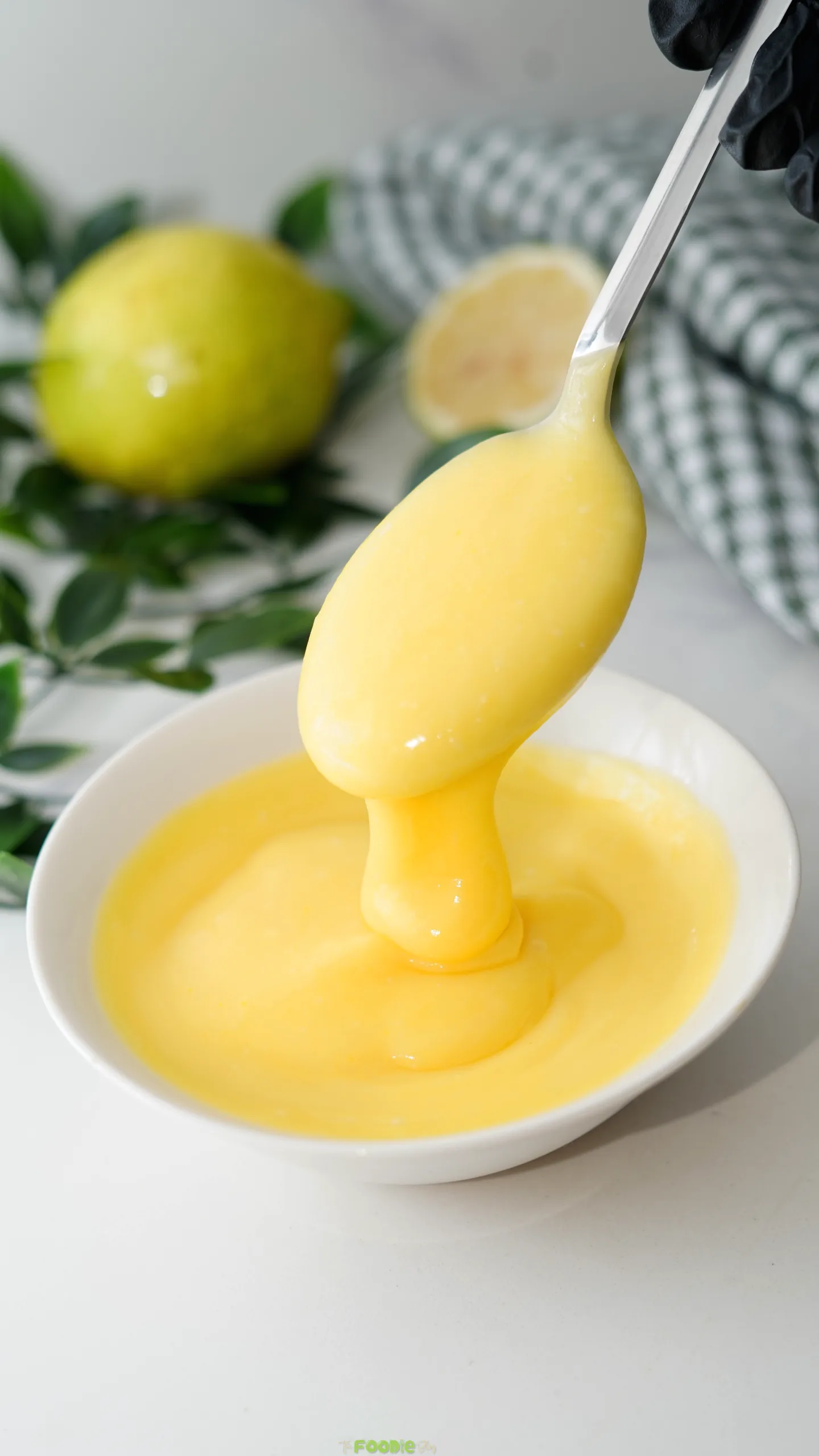 Creamy lime curd coating a spoon above a white bowl with fresh limes in the background.