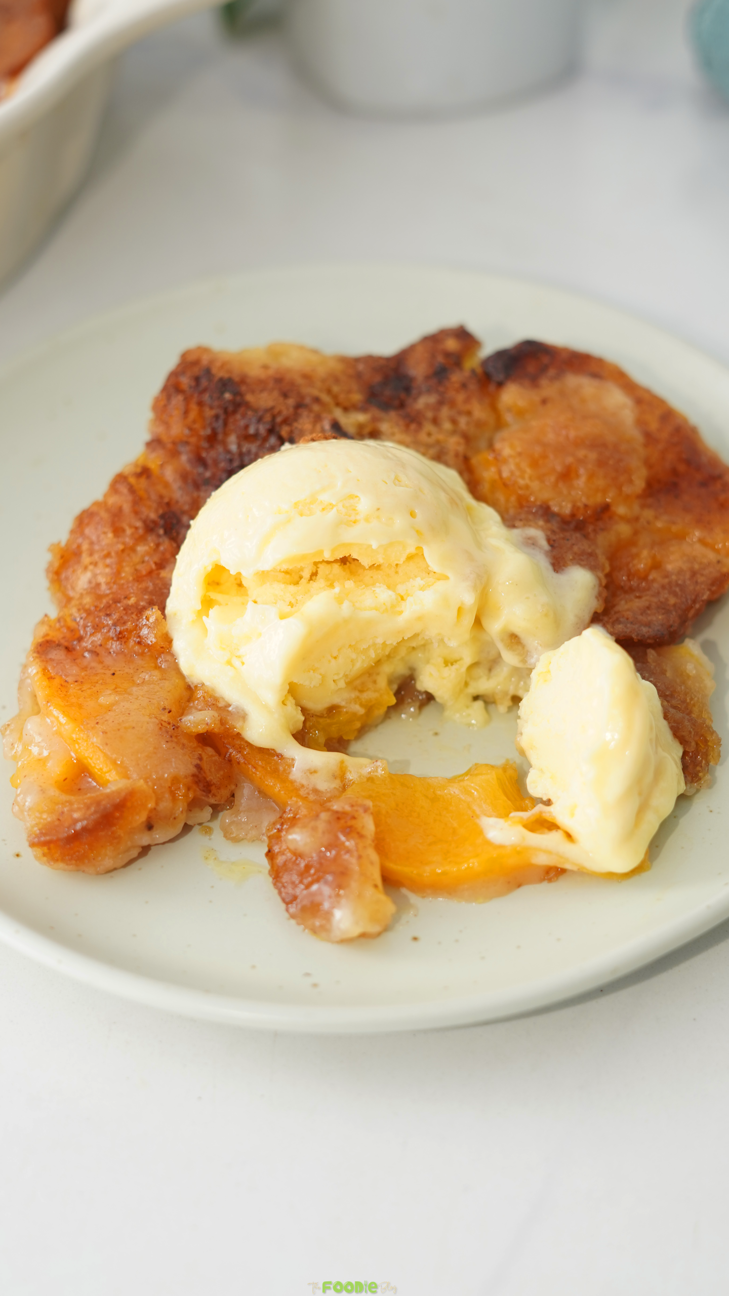 Golden canned peach cobbler baked in a white dish with soft peaches and a browned cake-style topping.