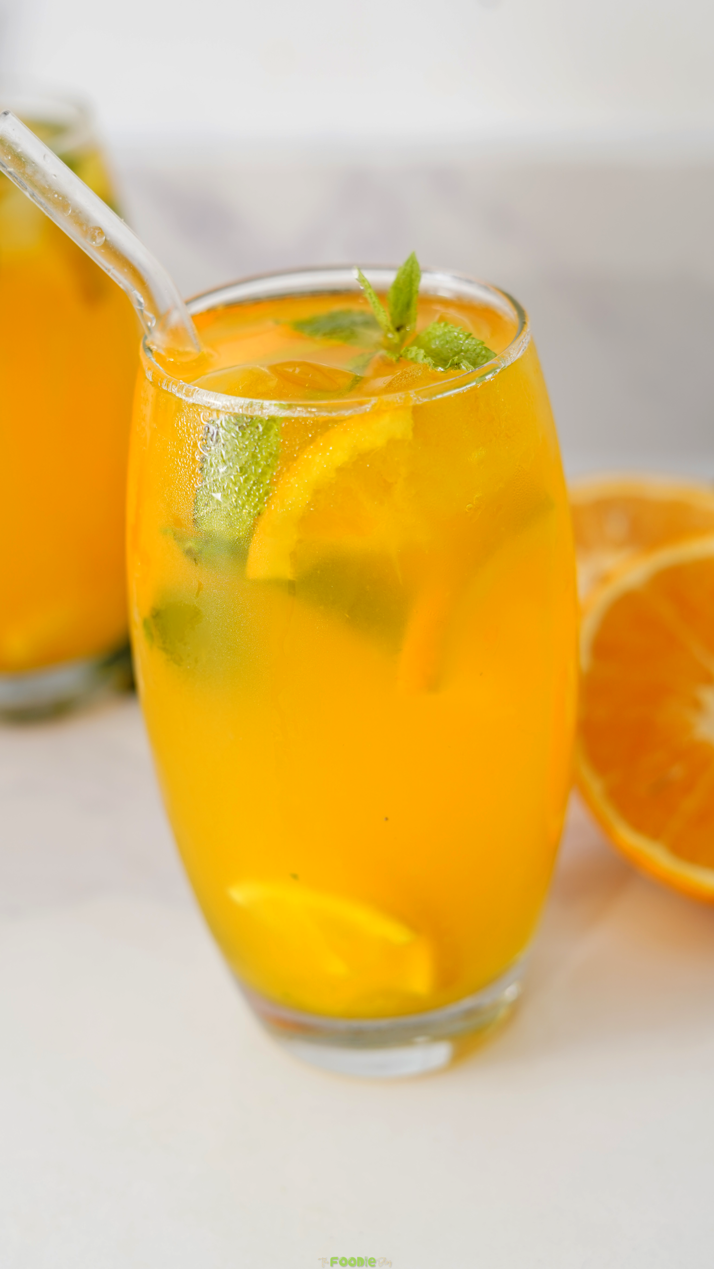 Close-up of a bright orange mojito with mint leaves, citrus slices, ice, and a glass straw.