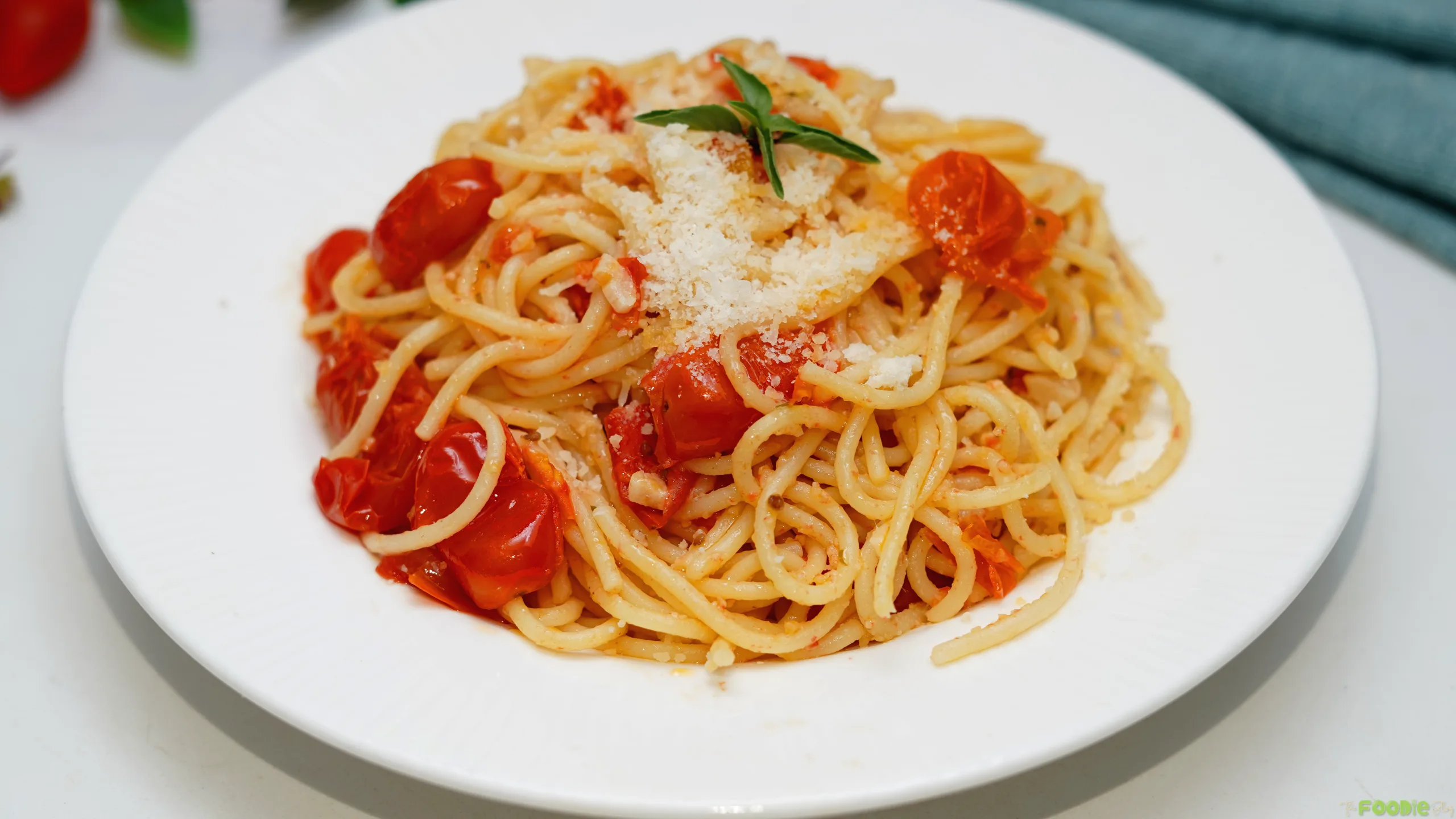 Fresh tomato pasta with spaghetti, cherry tomatoes, garlic, Parmesan, and herbs on a white plate.