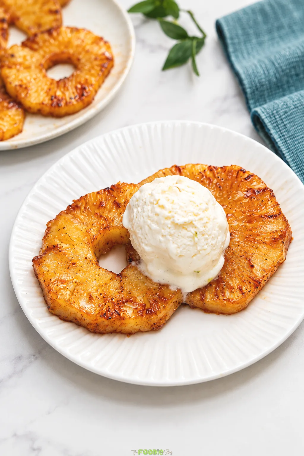 Two caramelized grilled pineapple rings topped with a scoop of vanilla ice cream.