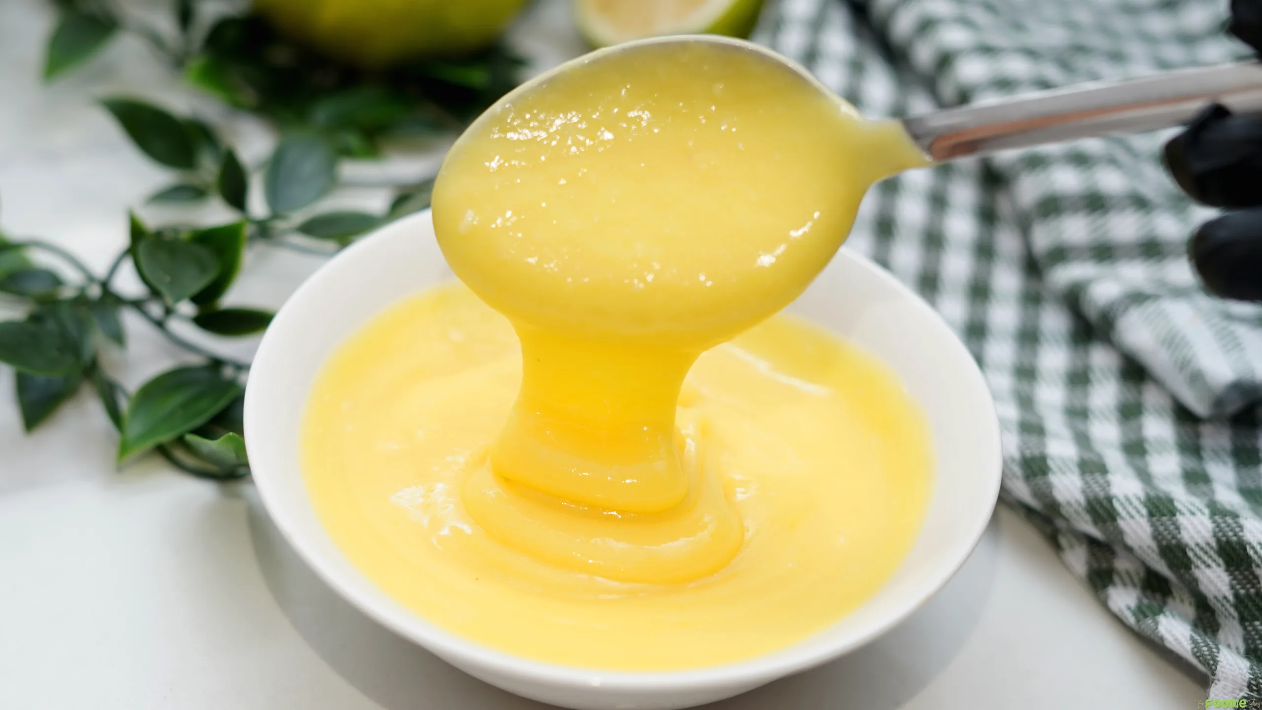 Smooth homemade lime curd dripping from a spoon into a white bowl.