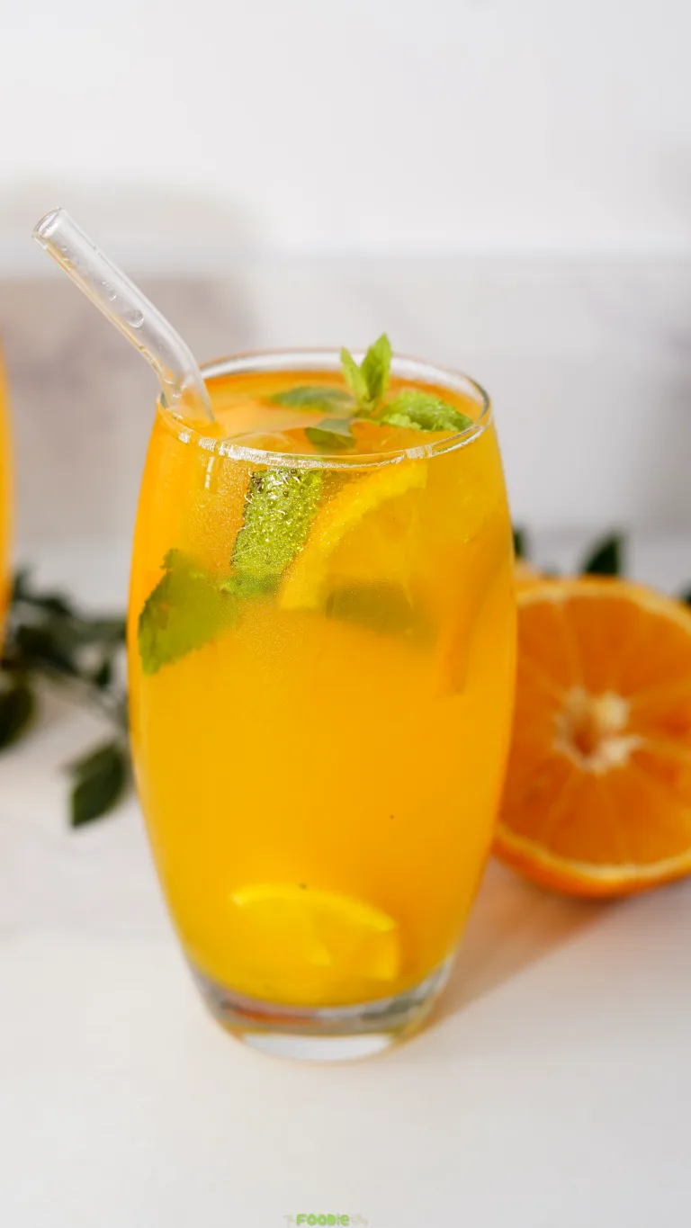 Cold orange vodka mojito with fresh mint, citrus slices, ice, and a glass straw.